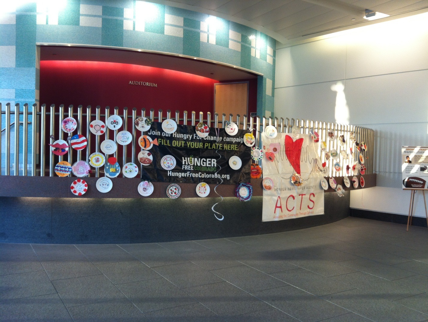 A Hunger Free Colorado banner and decorated paper plates at attached to a curved railing in an auditorium