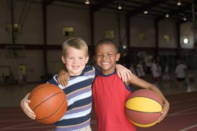 Two young boys stand, facing the camera, arm in arm and are holding basketballs against their outside hips