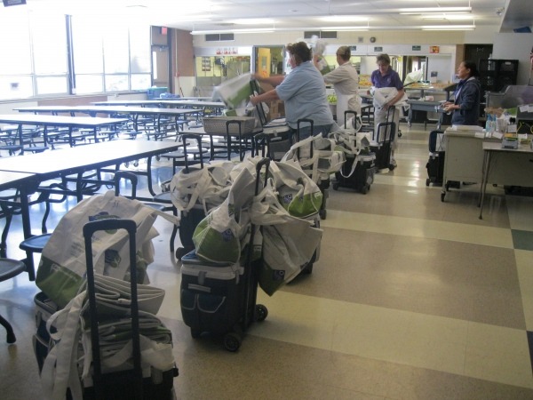 Adults prepare a line of blue rolling coolers topped with reusable bags
