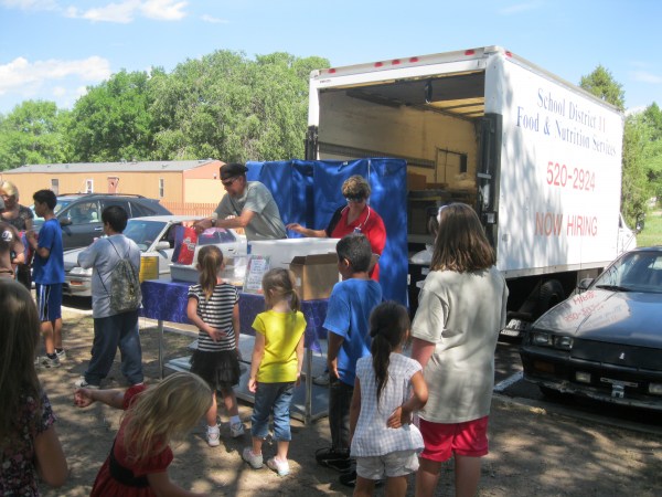 Nutrition Service professionals hand out food to kids waiting in line outside.