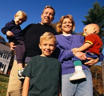 white family with three young boys, one is standing in front and two are being held on a parents hip