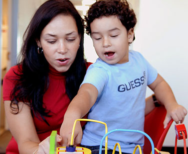 Woman in red shirt (left) plays with her son (right, blue GUESS shirt)