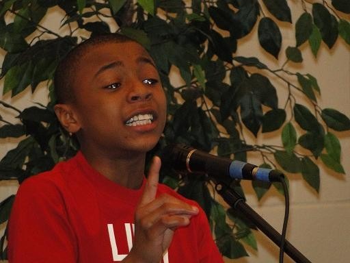 Young boy (in red shirt) speaks at a microphone