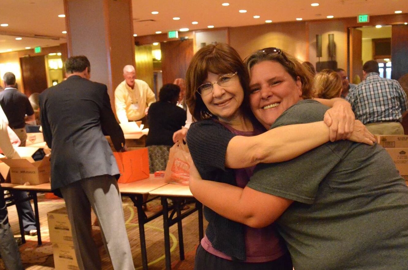 congrats two women hugging while people pack food in background