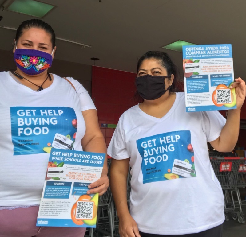 Two women doing p-ebt outreach holding informational flyers and wearing shirts that say "get help buying food"