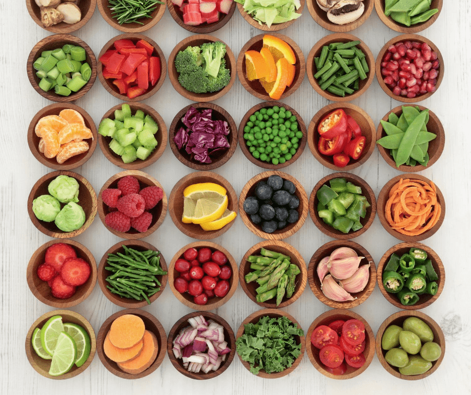 prepared veggies and fruits in brown wood bowls on a white wood plant background