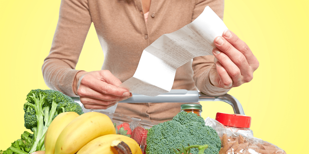 Woman in cardigan holds long, unfolded receipt over full grocery cart